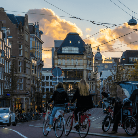 Two girls ride bikes down an Amsterdam street at dusk